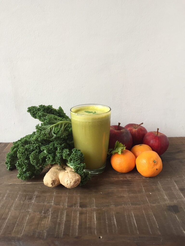 A green smoothie surrounded by kale, citrus fruit and fresh ginger