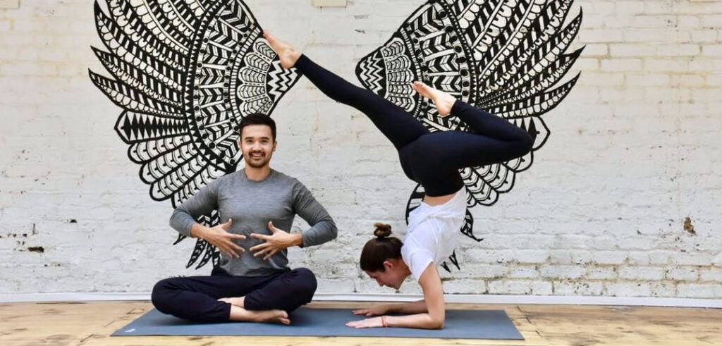 Two people practising partner yoga in front of a large winged mural