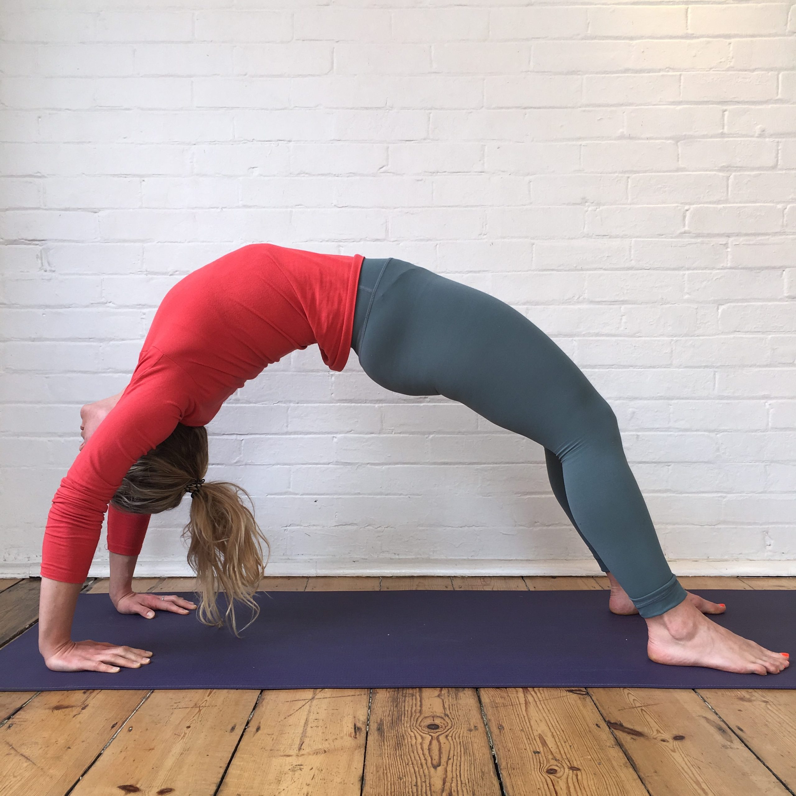 A woman in wheel pose on a wooden studio floor