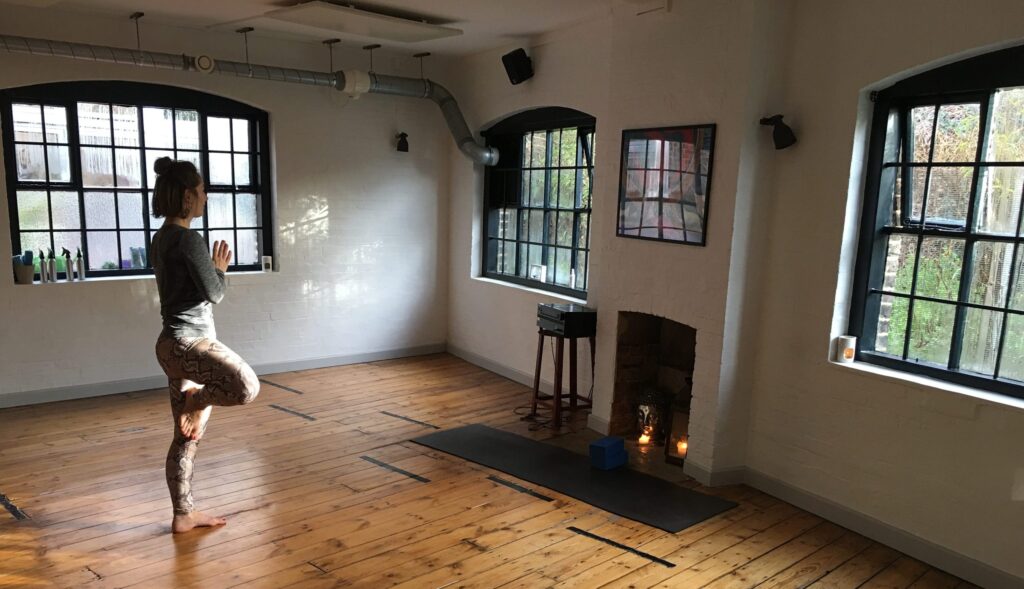 A yogi in tree pose in an empty studio with arched windows