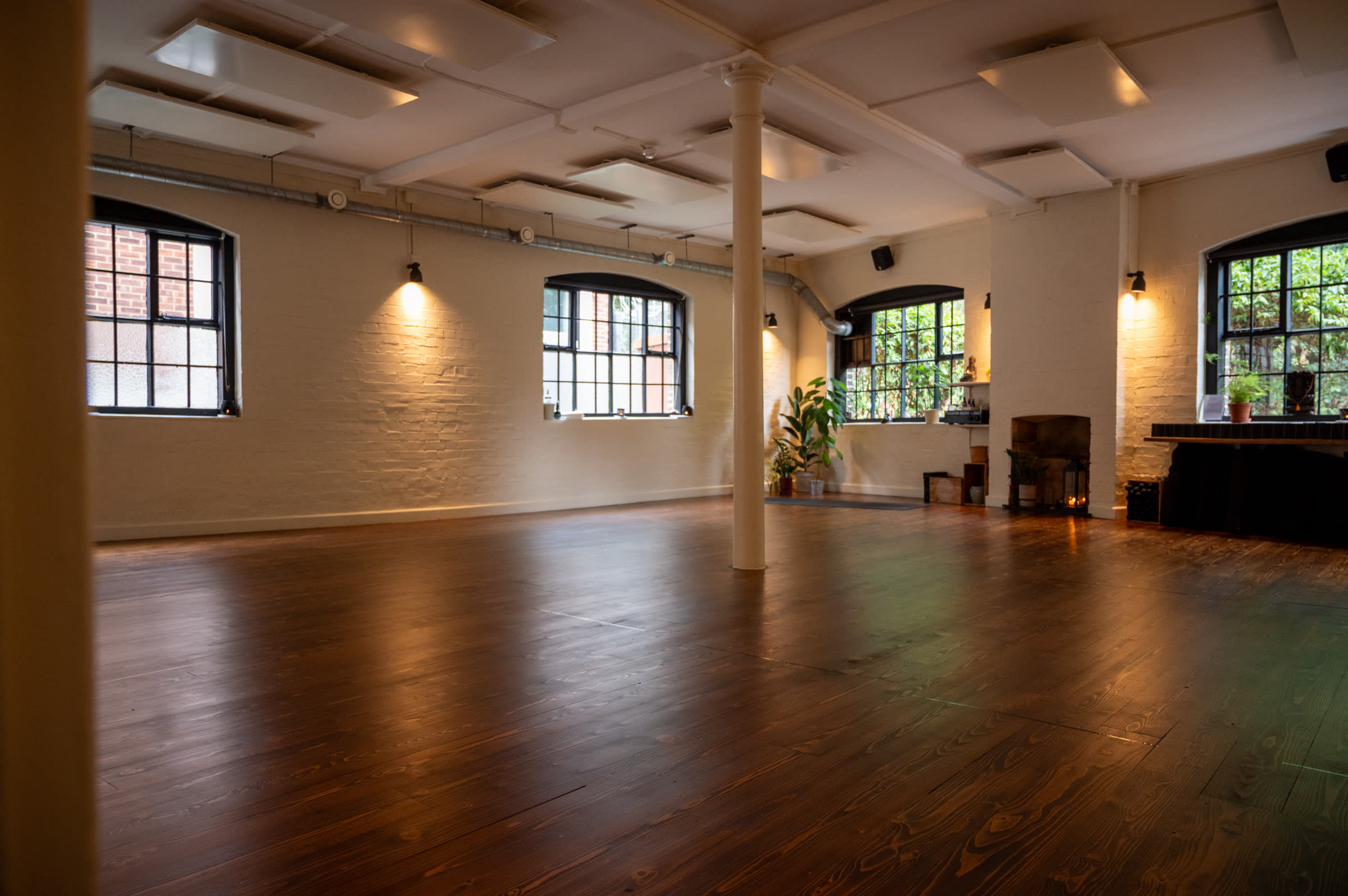 Mat studio with arched windows, wall lights and a dark wooden floor